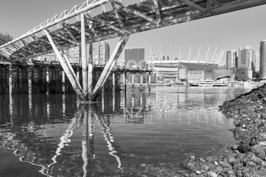False Creek seawall promenade and Vancouver skyline in black & white - View under the pedestrian footbridge with Vancouver skyline in the background - Olympic Village Square, Canada                               