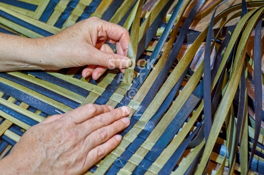 Flax weaving being made by hand - raranga harakeke - Closeup of the weaver’s hands making a kete - with property release from the artist