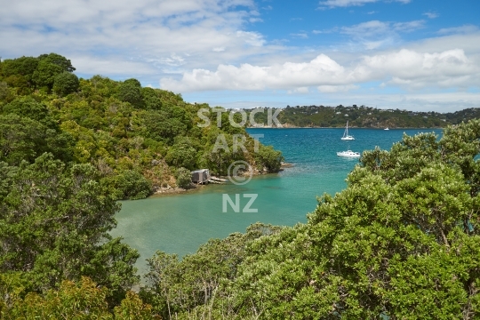 Oneroa Bay on Waiheke Island, off the Auckland coast, New Zealand - Boat sheds and boats seen from a walkway around the beach, lined with pohutukawa trees