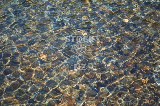 Rippling and glistening water surface - Crystal clear and very clean, shallow coastal water on a stony Marlborough Sounds beach                               